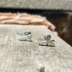 May include: A pair of silver earrings with a simple, minimalist design. Each earring features two thin, crossed bars.