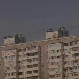 May include: A large, gray apartment building with many windows and balconies. The building has a flat roof and is made of concrete.