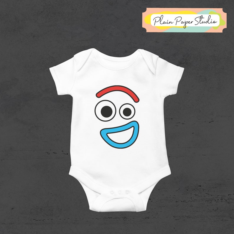 Pu&ograve; includere: Body da bambino bianco con un design a forma di viso di cartone animato. Il viso presenta una linea curva rossa sopra due cerchi neri per gli occhi e una bocca sorridente blu. Il testo "Plain Paper Studio" &egrave; su uno striscione in alto a destra.