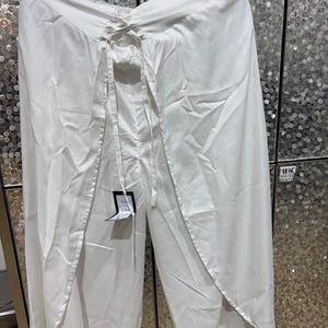May include: White palazzo pants with a wrap-style front and a drawstring waist. The pants are hanging on a black hanger. A tag is attached to the pants. The fabric appears to be lightweight and flowing.
