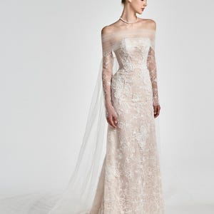 Könnte beinhalten: Elfenbeinfarbenes Hochzeitskleid mit floraler Spitze. Das schulterfreie Design hat transparente Ärmel und eine lange Schleppe. Die Braut trägt eine Perlenkette und passende Schuhe. Das Kleid ist bodenlang.