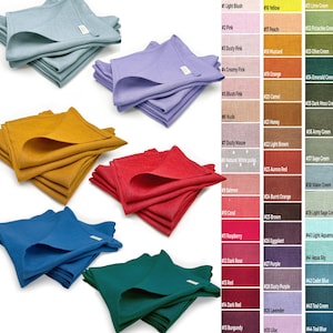 May include: Stacks of folded linen napkins in various colors, including blue, yellow, red, and green. Each napkin has a small tag. A color chart with names like "Light Blush" and "Mustard" is displayed.