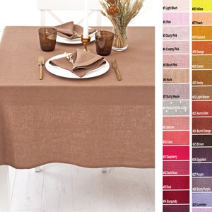 May include: A brown linen tablecloth is laid out on a white table. Two white plates with gold trim are set with napkins and glasses. The tablecloth is a natural linen color with a subtle texture.