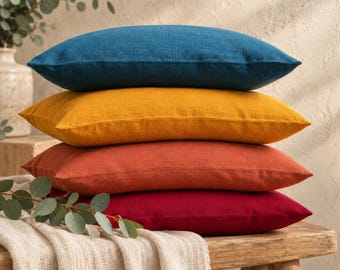 Op de afbeelding: Een stapel van vier rechthoekige sierkussens in effen kleuren, bestaande uit diepblauw, goudgeel, gebrand oranje en donkerrood. Elk kussen heeft een zichtbare geweven textuur en is horizontaal op elkaar gestapeld.