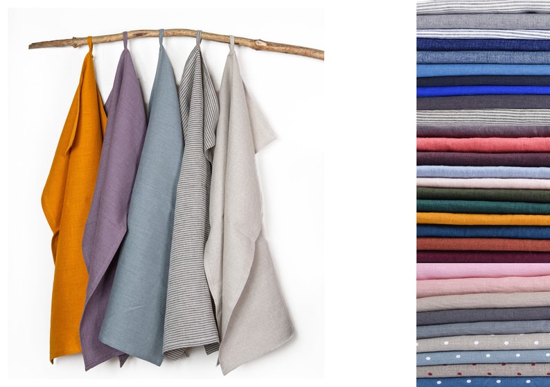 May include: Five linen kitchen towels hanging on a wooden branch. The towels are in various colors, including mustard yellow, purple, blue, gray with black stripes, and beige.