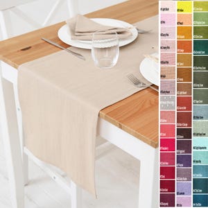 Può includere: Un runner da tavolo in lino beige su un tavolo di legno, con un tovagliolo e un piatto abbinati. Un bicchiere trasparente e posate sono anche sul tavolo. La tabella dei colori mostra varie opzioni di colore, tra cui rosa, rosso e verde.