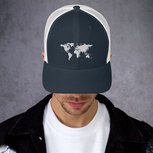 May include: A navy blue and white trucker hat with a white embroidered world map design.