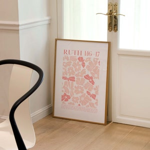 May include: A framed art print featuring a floral pattern in shades of pink and white, with the text "RUTH 1:16-17" at the top. The print is leaning against a white door with gold hardware, on a light wood floor.