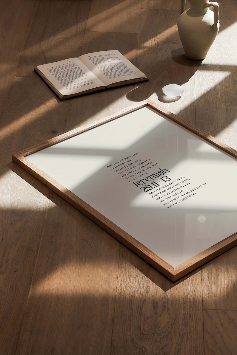Pu&ograve; includere: Una stampa incorniciata con il testo di Geremia 29:11-13 in nero. La stampa &egrave; in una cornice di legno marrone chiaro e poggia su una superficie di legno. Un libro aperto e un vaso bianco sono anche sulla superficie.