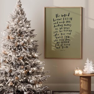 May include: A white flocked Christmas tree with gold and white ornaments and white lights. A framed print with the text "the word became flesh and made his dwelling among us. We have seen his glory the one and only son who came from the father full of grace and truth" is hanging on the wall. John 1:14 is printed at the bottom of the print.