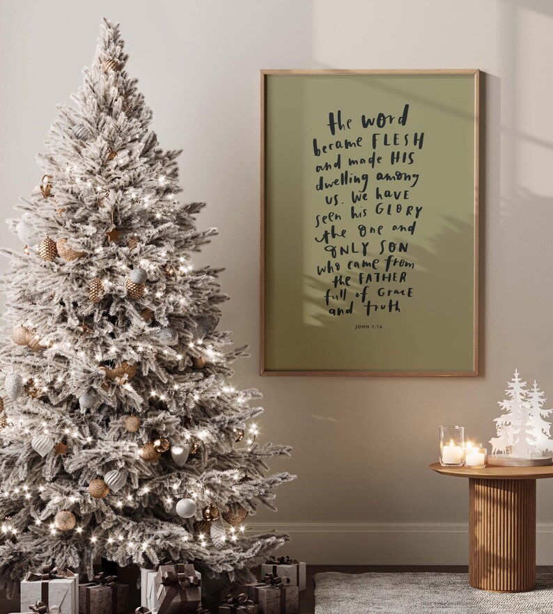 May include: A white flocked Christmas tree with gold and white ornaments and white lights. A framed print with the text "the word became flesh and made his dwelling among us. We have seen his glory the one and only son who came from the father full of grace and truth" is hanging on the wall. John 1:14 is printed at the bottom of the print.