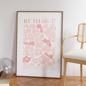 May include: A framed art print featuring a floral design in shades of pink. The print includes the text "RUTH 1:16-17" at the top and a passage below. The artwork is displayed on a white wall, next to a chair.