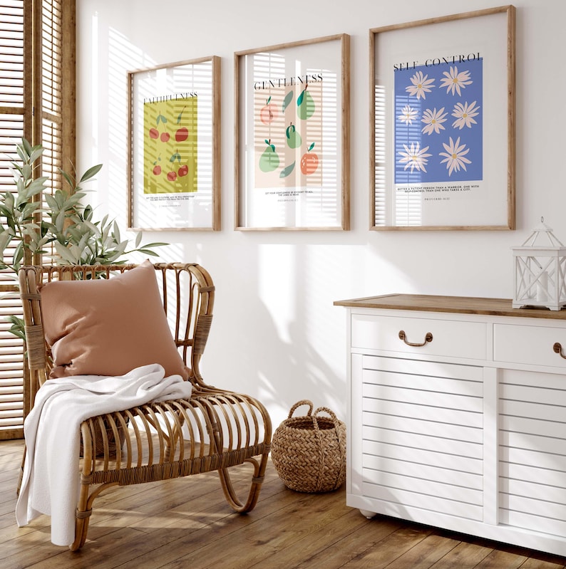 Puede incluir: Tres impresiones art&iacute;sticas enmarcadas con ilustraciones bot&aacute;nicas y texto, incluyendo "SELF CONTROL" y "GENTLENESS". Una silla de mimbre con un coj&iacute;n color melocot&oacute;n y una manta blanca se encuentra cerca de un mueble blanco y una cesta de mimbre. La habitaci&oacute;n tiene persianas de madera.