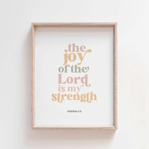 May include: A framed print with the text "the joy of the Lord is my strength" in various pastel colors. The print is in a light wood frame and includes the reference "NEHEMIAH 8:10" at the bottom. The background is white.