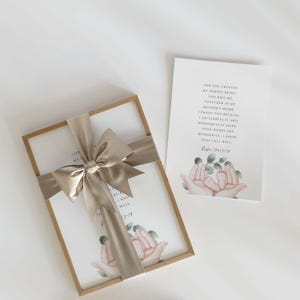 May include: A framed print with a watercolor illustration of two tiny feet in cupped hands. The print has a beige background with green leaves and the text "For you created my inmost being, you knit me together in my mother's womb. I praise you because I am fearfully and wonderfully made. Your works are wonderful, I know that full well. Psalm 139:13-14". The print is wrapped in a brown frame and tied with a beige satin ribbon.