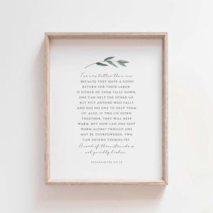 Op de afbeelding: Een ingelijst print met een witte achtergrond en zwarte tekst. De tekst luidt: "Twee zijn beter dan één, want zij hebben een goede beloning voor hun arbeid. Als een van hen valt, kan de ander hem helpen op te staan. Maar heb medelijden met degene die valt en niemand heeft om hem te helpen opstaan. Evenzo, als twee samen liggen, zullen ze warm blijven. Maar hoe kan iemand warm blijven, hoewel hij overweldigd kan worden, twee kunnen zichzelf verdedigen. Een touw van drie strengen scheurt niet snel. Prediker 4:9-12"