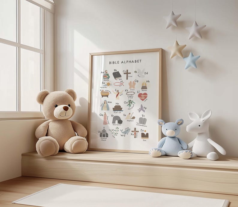 May include: A framed "Bible Alphabet" print with colorful illustrations and text, next to a plush teddy bear, a blue bear, and a white bunny. Decorative star-shaped ornaments hang from the ceiling. The scene is set in a bright room.