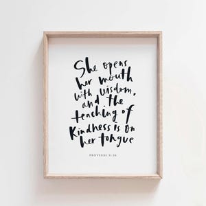 May include: A framed print with a black and white inspirational quote from Proverbs 31:26. The quote reads "She opens her mouth with wisdom, and the teaching of kindness is on her tongue".