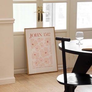 May include: A framed print with a pink floral pattern and the text "JOHN 15:12" in red. The text below the floral pattern reads "Love each other as I have loved you."