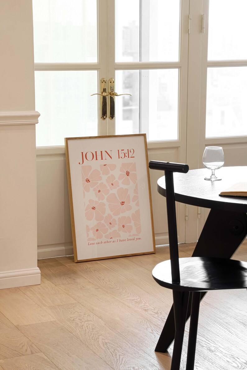 May include: A framed print with a pink floral pattern and the text "JOHN 15:12" in red. The text below the floral pattern reads "Love each other as I have loved you."