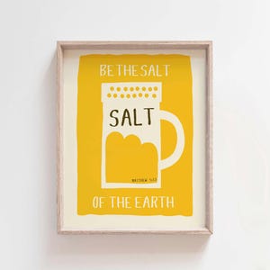 May include: A yellow and white framed print with the text "Be the salt of the earth" and a graphic of a salt shaker with the word "SALT" on it. The text "Matthew 5:13" is also included.
