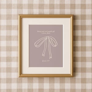 Pode incluir: Uma impressão emoldurada com um fundo roxo claro e um contorno branco de um laço. O texto "Every good and perfect gift is from above" está escrito em branco acima do laço. O texto "James 1:17" está escrito em branco abaixo do laço.