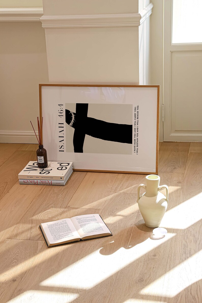 May include: A framed black and white print with the text "ISAIAH 46:4 I HAVE MADE YOU AND I WILL CARRY YOU: I WILL SUSTAIN YOU AND I WILL RESCUE YOU."  The print is sitting on a wooden floor with a white vase and three books.