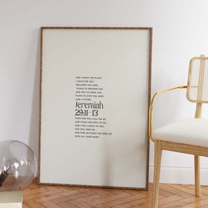 Pu&ograve; includere: Stampa incorniciata con il testo di Geremia 29:11-13 in nero su sfondo crema. La cornice &egrave; in legno scuro. Una sedia moderna con struttura dorata e un globo di vetro sono sullo sfondo. Il pavimento &egrave; in legno.