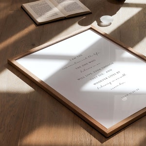 May include: A framed print with a white background and black text. The text reads "I am the resurrection and the life. The one who believes in me will live, even though they die: and whoever lives by believing in me will never die. John 11:25-26"