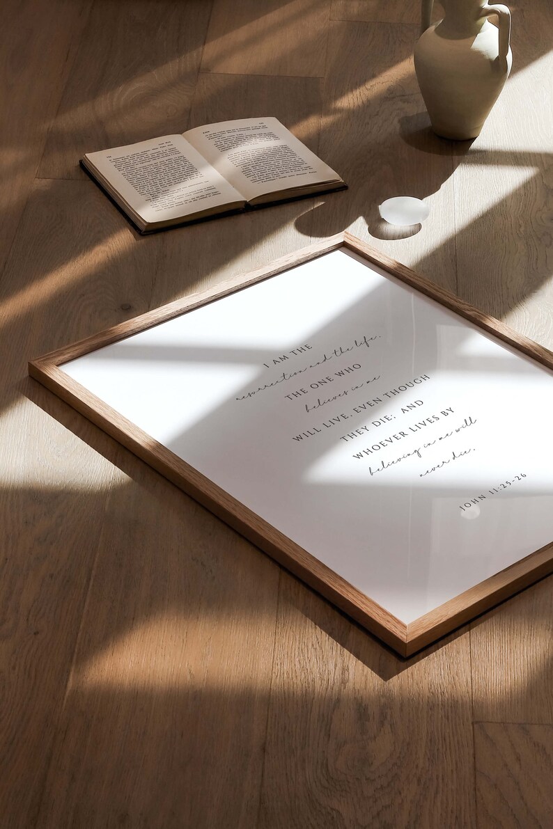 May include: A framed print with a white background and black text. The text reads "I am the resurrection and the life. The one who believes in me will live, even though they die: and whoever lives by believing in me will never die. John 11:25-26"