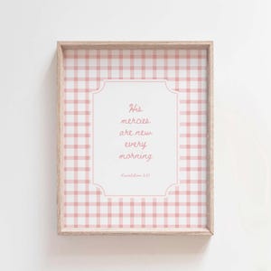Op de afbeelding: Een ingelijst wandkunstwerk met een roze en wit gingham-patroon met de quote "Zijn genaden zijn elke morgen nieuw" en de bijbelverwijzing "Klaagliederen 3:23".