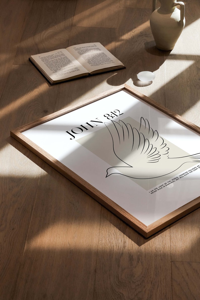 May include: A framed print with a white background and a black line drawing of a dove. The text "JOHN 8:12" is in black at the top of the print. The quote "I am the light of the world. Whoever follows me will never walk in darkness, but will have the light of life." is in black at the bottom of the print.