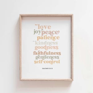 May include: A framed print with a white background and a list of words in different colors: love, joy, peace, patience, kindness, goodness, faithfulness, gentleness, self-control. The words are in a retro font style. The text "GALATIANS 5:22-23" is at the bottom of the print.