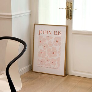 May include: A framed print with a floral design in shades of pink and red. The print features the text "JOHN 15:12" and the quote "Love each other as I have loved you."