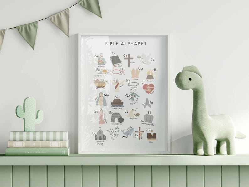 May include: A framed "Bible Alphabet" print with colorful illustrations of biblical themes. A green dinosaur figurine and a cactus-shaped decoration sit on a shelf with books. A garland of green triangles hangs above.