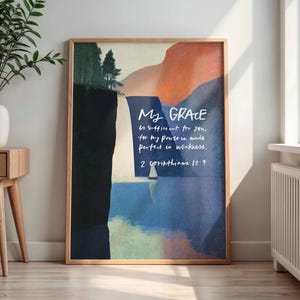 May include: A framed art print with a landscape design. The artwork features a color palette of blue, orange, and green. Text in white script reads "My GRACE is sufficient for you, for my power is made perfect in weakness. 2 Corinthians 12:9."