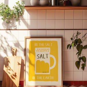 May include: A framed print with a yellow background and white text that reads "Be the salt, Salt, Matthew 5:13, Of the Earth". The print features a stylized illustration of a salt shaker.