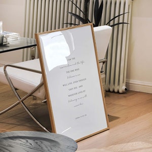 May include: A framed print with a white background and black text. The text reads "I am the resurrection and the life. The one who believes in me will live, even though they die: and whoever lives by believing in me will never die." John 11:25-26