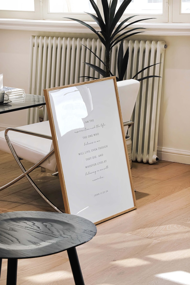 May include: A framed print with a white background and black text. The text reads "I am the resurrection and the life. The one who believes in me will live, even though they die: and whoever lives by believing in me will never die." John 11:25-26