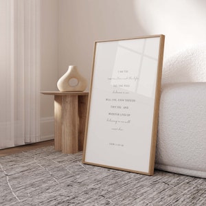 May include: A framed print with a white background and black text. The text reads "I am the resurrection and the life. The one who believes in me will live, even though they die. And whoever lives by believing in me will never die." John 11:25-26