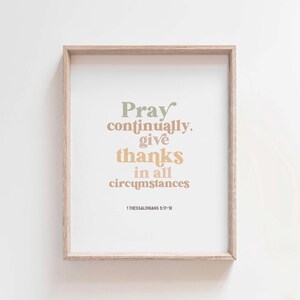 May include: A framed print with a beige background and a quote in various shades of brown, green, and pink. The quote reads "Pray continually, give thanks in all circumstances" with the scripture reference "1 Thessalonians 5:17-18" at the bottom.