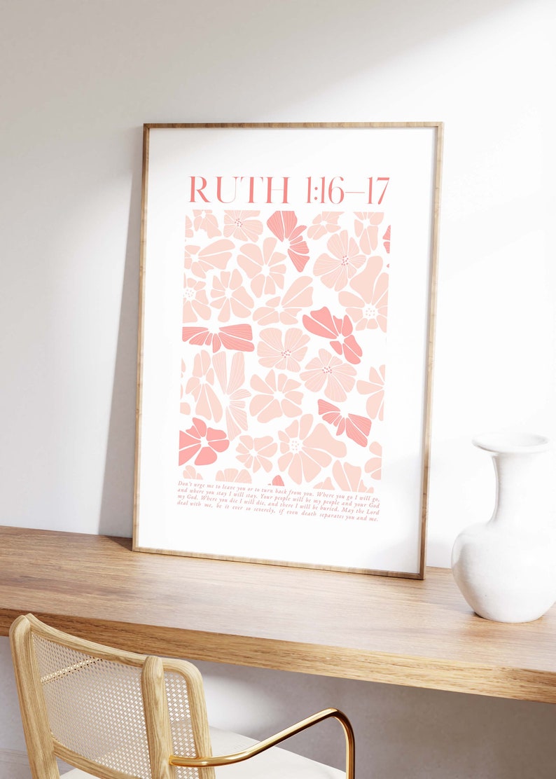 May include: A framed art print featuring a floral design in shades of pink. The print includes the text "RUTH 1:16-17" at the top and a passage below. The artwork is displayed on a wooden surface.