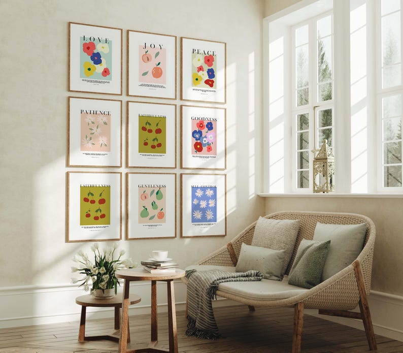 Puede incluir: Nueve impresiones art&iacute;sticas enmarcadas con ilustraciones bot&aacute;nicas y palabras inspiradoras como "Amor" y "Alegr&iacute;a" cuelgan de una pared. Las impresiones presentan flores coloridas, frutas y dise&ntilde;os sencillos. Un sof&aacute; de mimbre con cojines y una peque&ntilde;a mesa de madera est&aacute;n frente a una ventana.