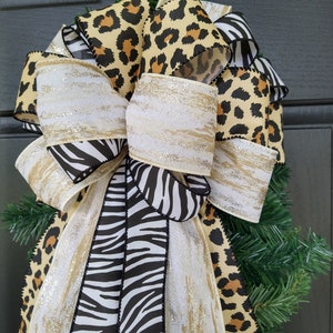 May include: A Christmas tree topper bow made with leopard print, zebra print, and white ribbon with gold glitter. The bow is tied with a large, fluffy knot.