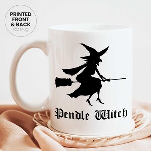 May include: White ceramic mug with a black silhouette of a witch on a broomstick, with the words "Pendle Witch" in a gothic font. The mug has a curved handle and the text "PRINTED FRONT & BACK 11oz Mug".