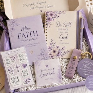 May include: A gift box containing a lavender Mini Faith Devotional book, a spiral-bound journal with floral accents and the text Be Still and Know That I Am God, a matching pen, a sticker pack, a square card, a keychain, and a candle with text.