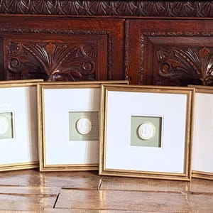 Può includere: Quattro opere d'arte incorniciate con cornici dorate. Ogni cornice contiene un passe-partout bianco con un'apertura quadrata, che rivela uno sfondo verde chiaro e una scultura a rilievo circolare bianca. Le cornici sono allineate.