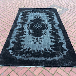 Puede incluir: Una alfombra vintage negra y azul con un patrón floral. La alfombra tiene un aspecto descolorido y está hecha de un material suave.