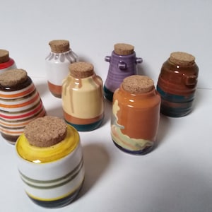 Può includere: Una collezione di otto barattoli in ceramica con coperchi in sughero. I barattoli sono decorati con vari motivi e colori, tra cui strisce, vortici e disegni astratti. I barattoli sono tutti di dimensioni e forme diverse.