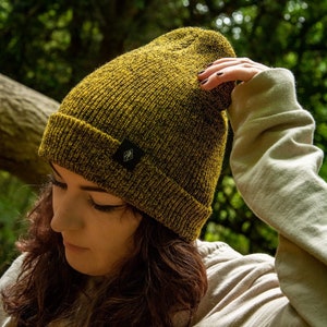May include: A person wearing a yellow and black knitted beanie with a small black logo on the side. The beanie is pulled down over their forehead and they are looking down.